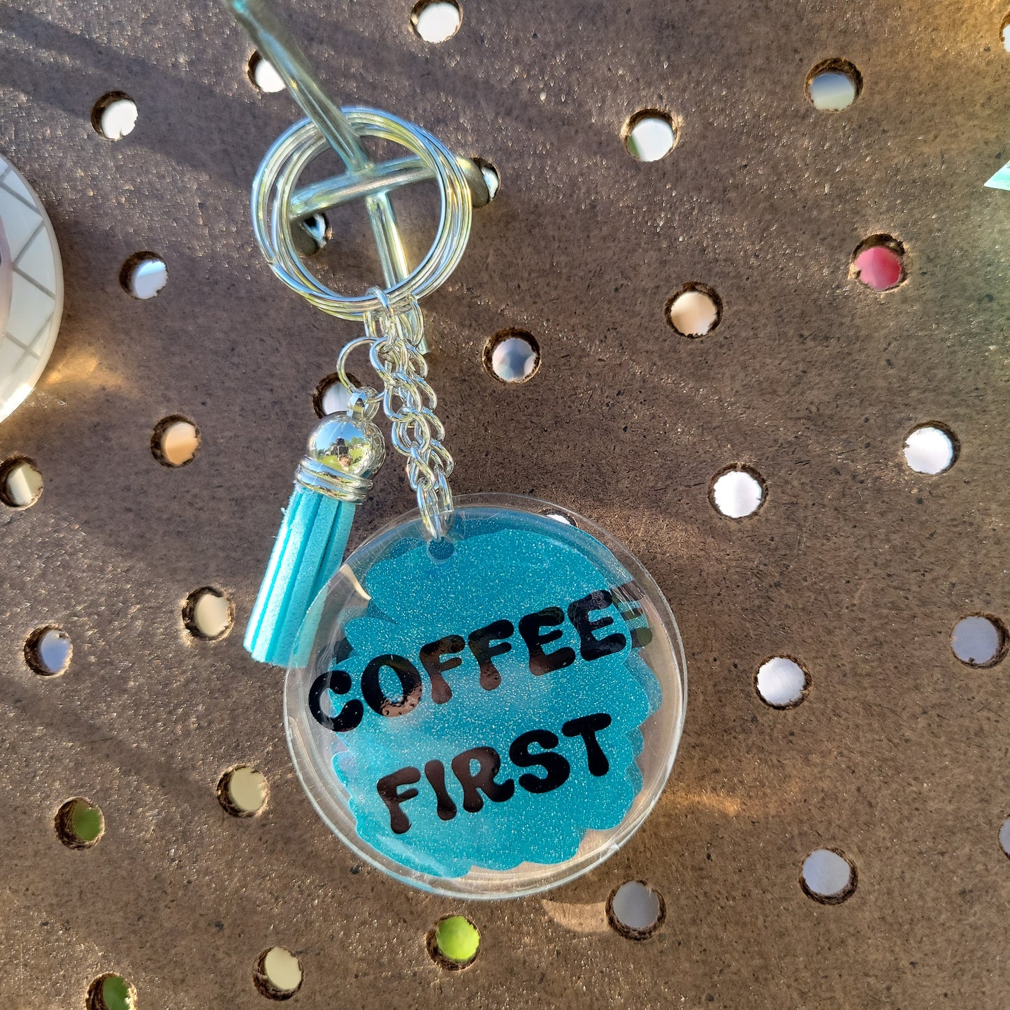 A blue keychain with the text 'COFFEE FIRST' written in black letters, attached to a metal keychain loop.